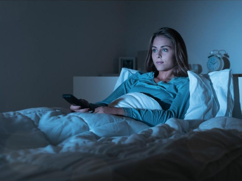 Woman in bed binge-watching nightime TV.